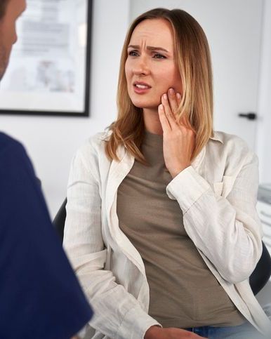 Patient holding her jaw in discomfort while consulting with a dentist